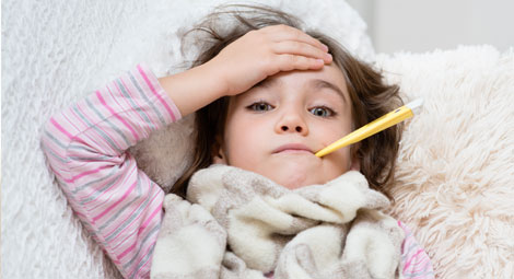 A young girl with a thermometer in her mouth touching her forehead